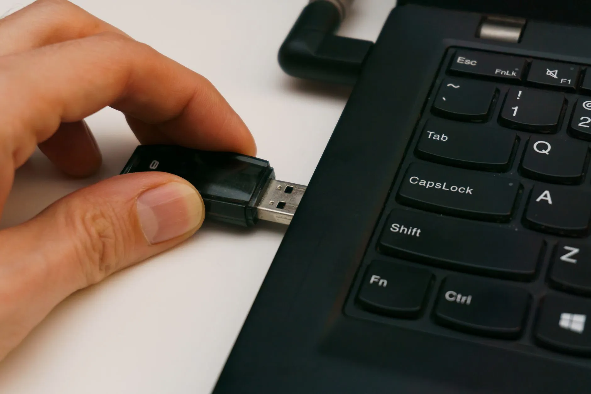 Mão encaixando um dispositivo USB na porta lateral de um notebook