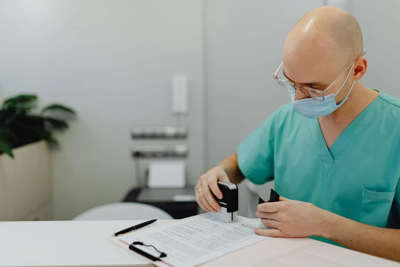 Médico de máscara e roupa cirúrgica carimbando um documento na mesa da clínica