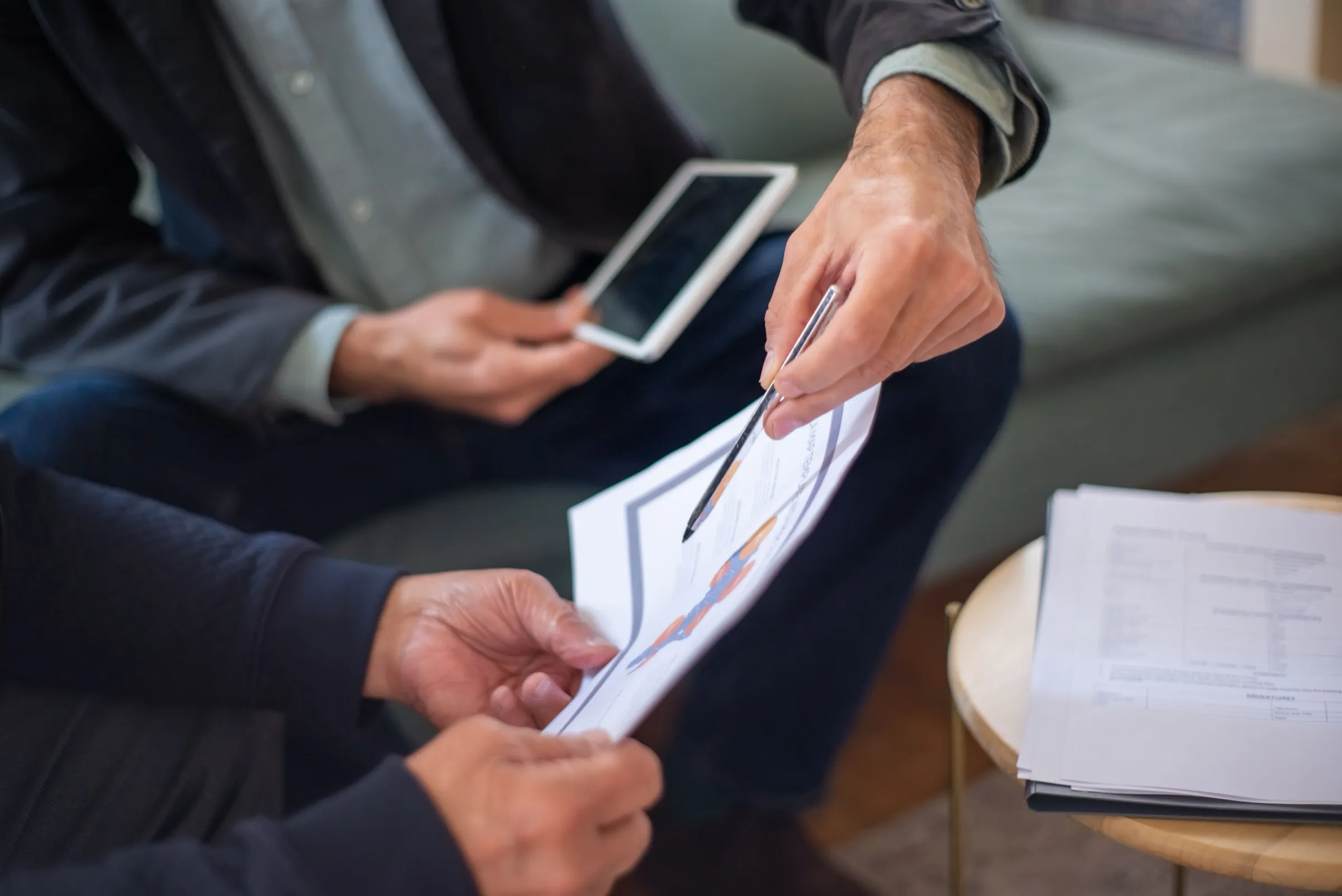 Duas pessoas conferindo documentos com gráficos durante uma reunião, uma delas apontando um item com a caneta