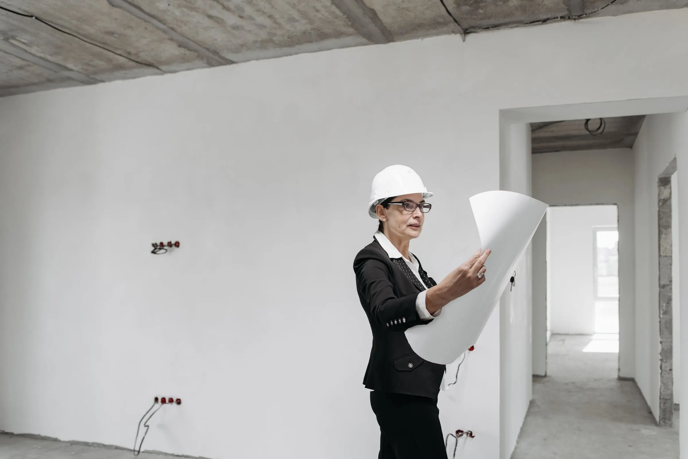 Engenheira de capacete branco conferindo uma planta dentro de um imóvel em obra