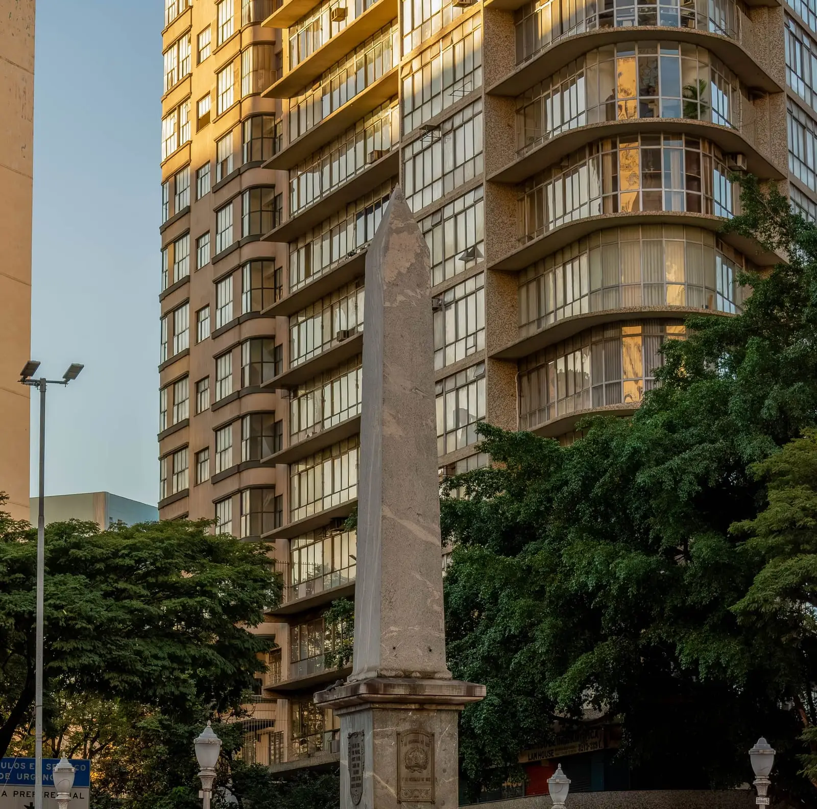 Obelisco da Praça Sete de Setembro, no Centro de Belo Horizonte, diante de um prédio de varandas curvas no fim da tarde